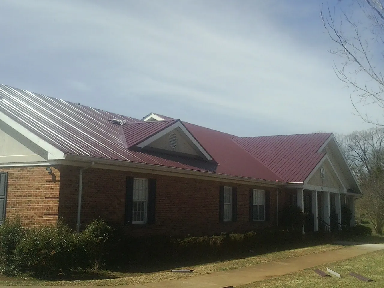 Red metal roof with gabled entries on a long brick building, from a Hail Damage Roof Repair job in Rowley