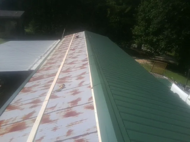 Old rusted panels beside newly installed green metal roofing — Wind Damage Roof Repair by Roofing Brothers in Rowley
