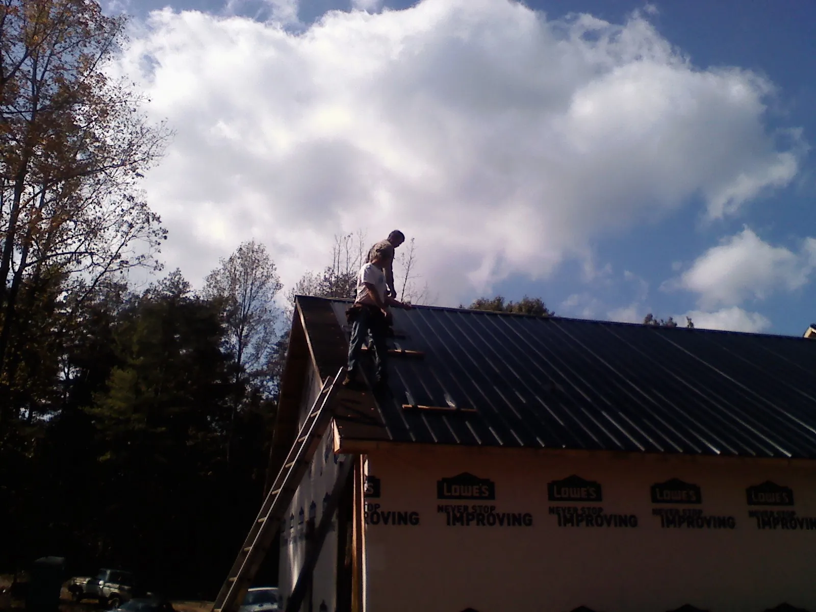 Roofer fastening dark metal panels high against a cloudy sky, from a Roof Inspection job in Rowley